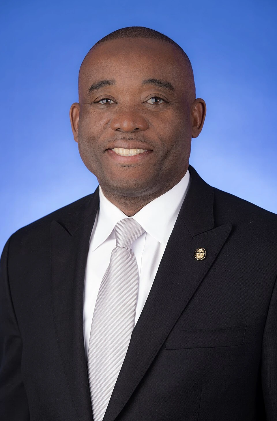 Jean Monestime portrait in suit and tie against a blue background