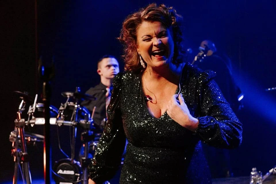 Jeanick Fournier singing on stage in a black sequined dress with a band behind her