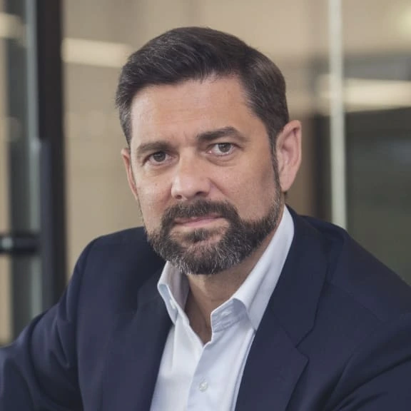 Portrait photo of Laurent Uberti in a navy suit and white shirt, seated indoors and looking at the camera